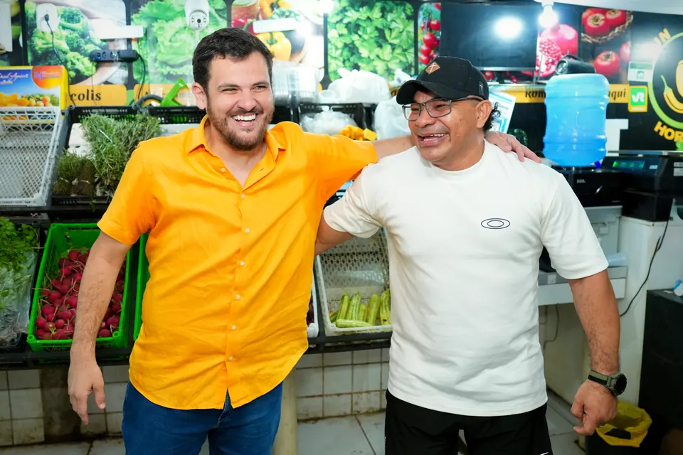 Renato Junior com um feirante entre bancas de frutas e verduras