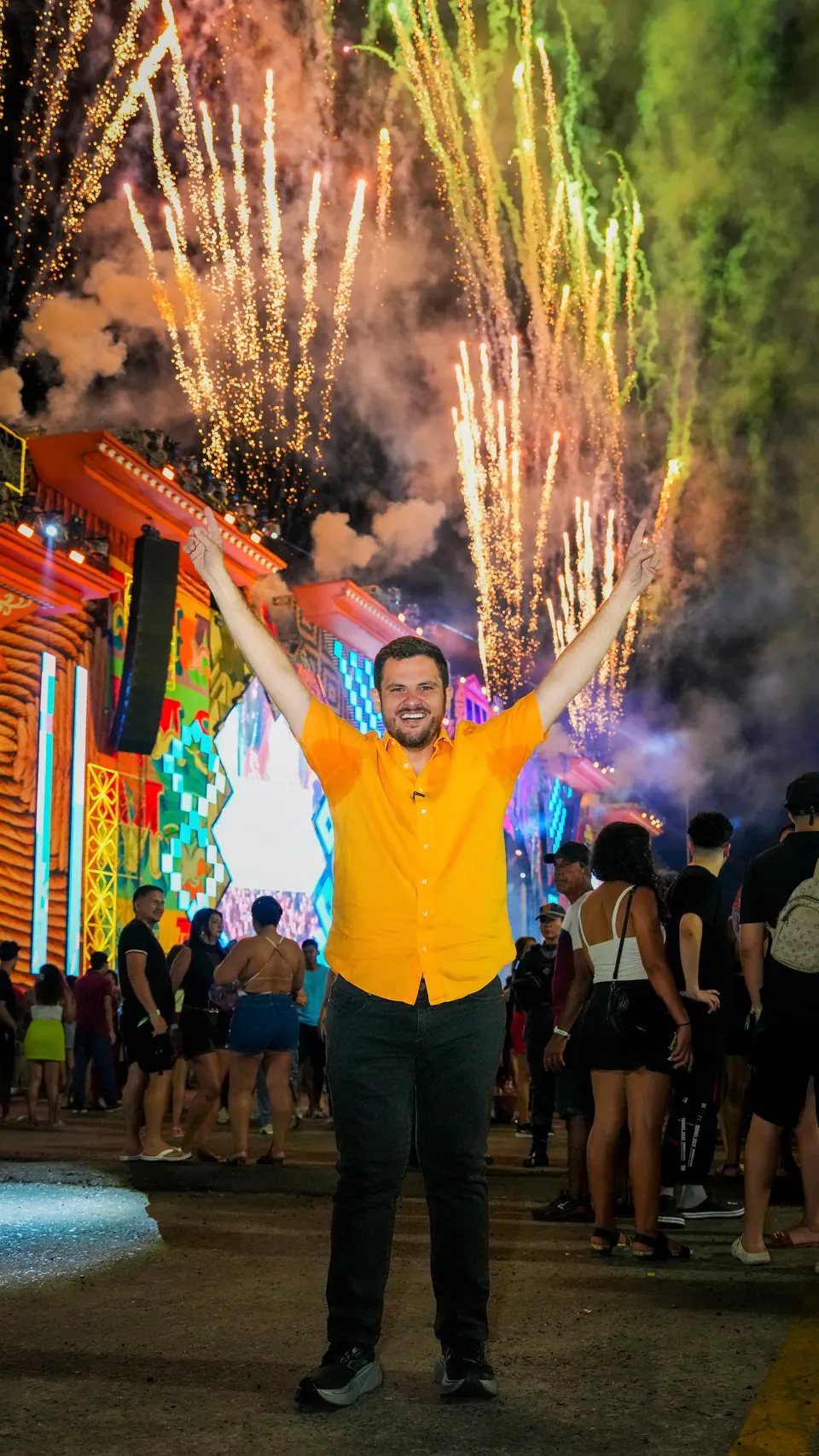 Renato Junior ergue os braços diante de fogos de artifício em um evento à noite