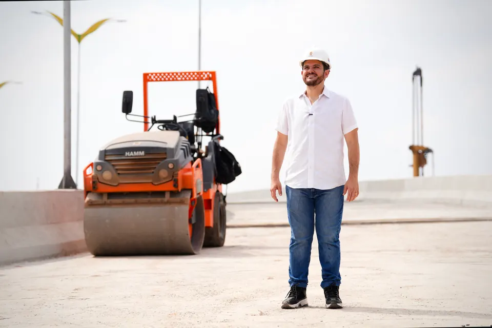 Renato Junior, de capacete, ao lado de um rolo compactador em obra
