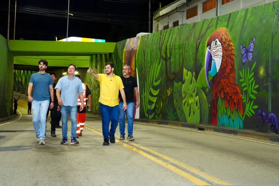 Renato Junior caminha à noite com a equipe por uma passagem com mural de araras